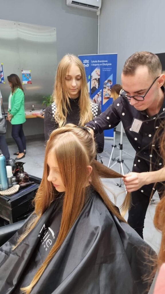uczeń szkoły fryzjerskiej wykonuje strzyżenie damskie