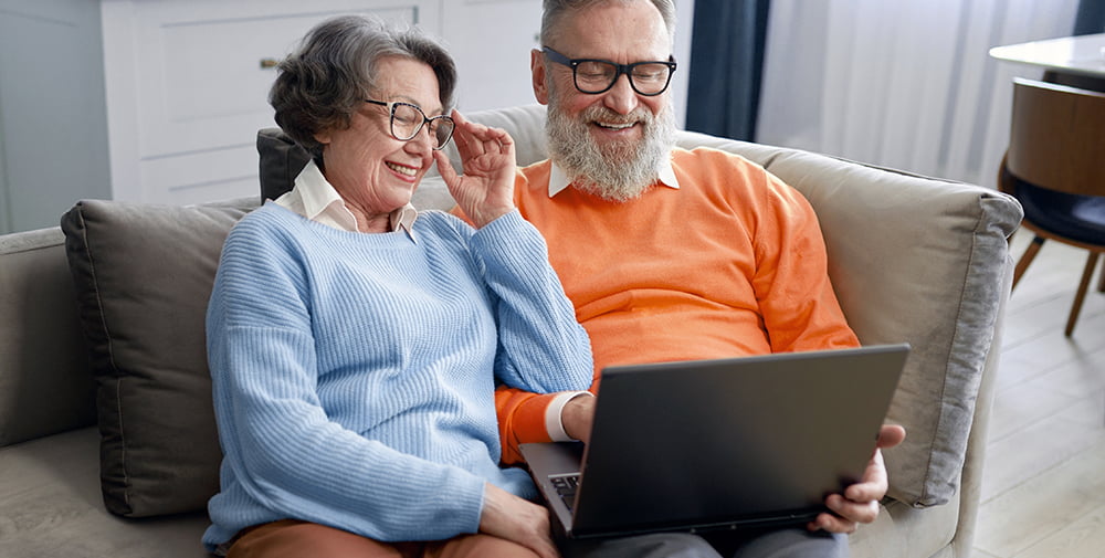 dwoje uśmiechniętych seniorów przed ekranem laptopa