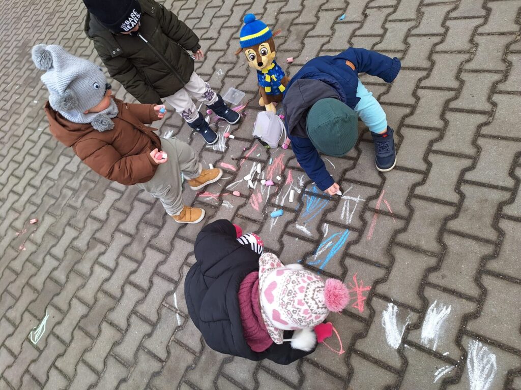 dzieci malują kolorową kredą po chodniku